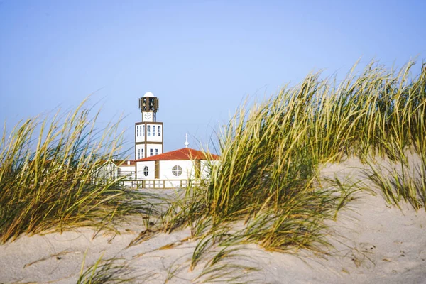 Costa nova church and tower naturally framed with beach sand dunes and sea oats during daylight. Royalty Free Stock Images