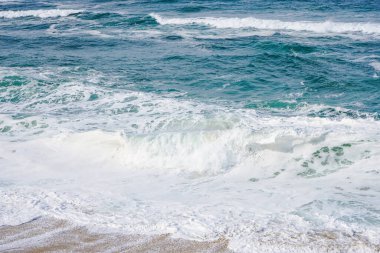 Turkuaz okyanus suyu ve küçük beyaz köpük dalgaları yavaşça altın kumsala çarpıyor.