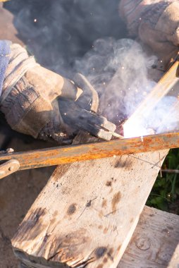 Kaynak demiri. İşçi demir parçaları kaynaklıyor. Araçlarla dolu bir palette çalışma yeri.