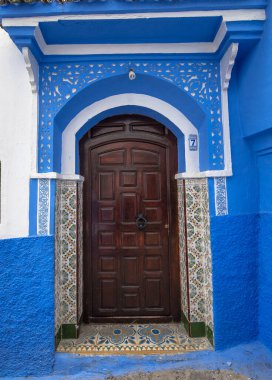 Tipik, eski, karmaşık bir şekilde oyulmuş, çivili, Fas Riad kapısı, kapı çerçevesi ve eski ev. Medine 'deki mavi şehrin güzel manzarası. CHEFCHAOUEN, FOCCO 'da boyalı evler
