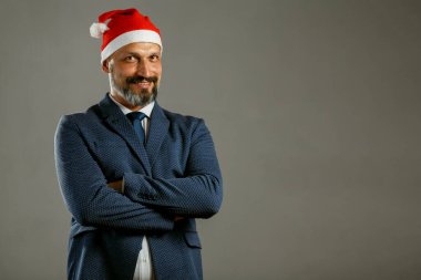 Mavi ceketli sakallı adam ve gri arka planda bir Noel şapkası.