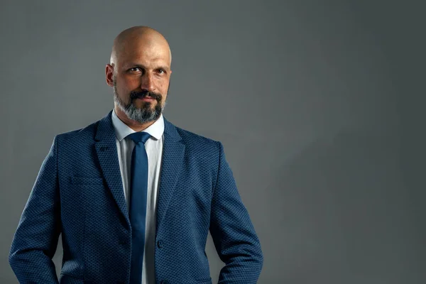 Kopya alanı ile gri bir arka plan üzerinde klasik bir takım elbise brutal kel sakallı işadamı