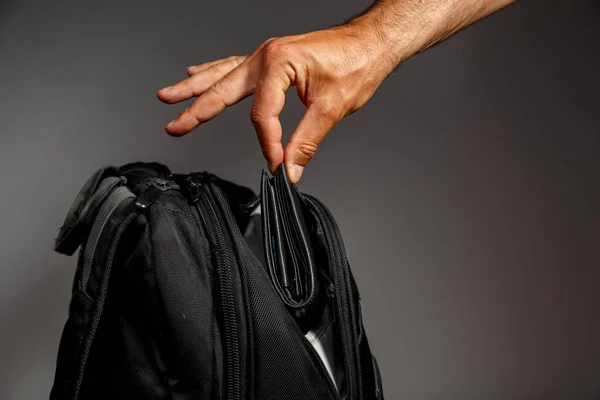 Thief\'s hand pulls a purse from a backpack on a gray background