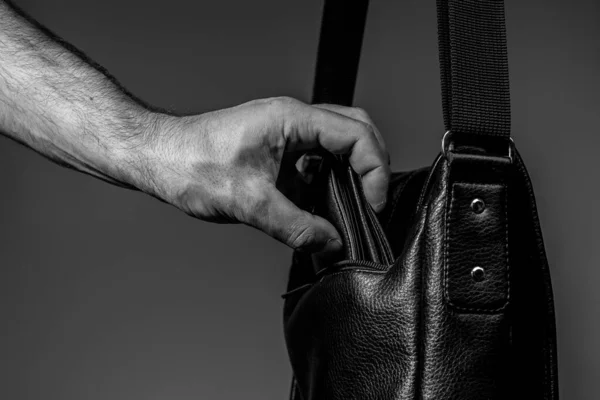 Foto em preto e branco da mão de um ladrão puxando uma bolsa de um saco de couro em um fundo cinza — Fotografia de Stock