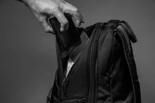一个小偷的手从灰色背景的背包里掏出钱包的黑白照片 — 图库照片