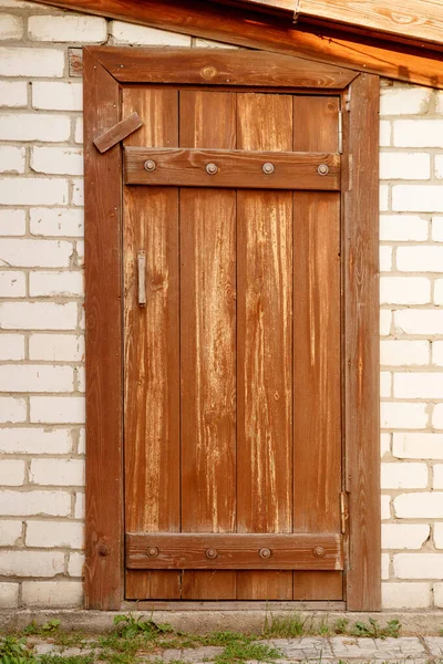Vieille porte en bois sale et sale recouverte de peinture brune. Avec une poignée et une constipation insérées dans un mur de briques de silicate blanc . — Photo