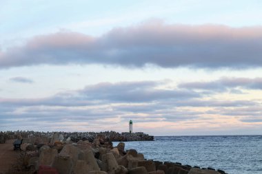 Güneş doğarken deniz manzarası ve arka planda bir deniz feneri.