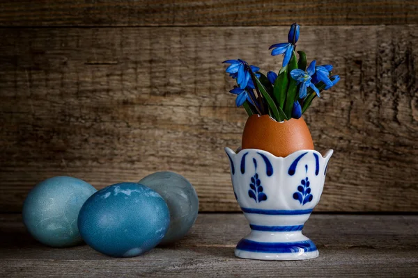 Paassamenstelling Met Blauwe Sneeuwklokjes Een Eierstatief Gekleurde Eieren Een Houten — Stockfoto