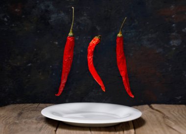 Üç kırmızı kuru kırmızı biber beyaz bir tabağın üzerinde uçuyor.