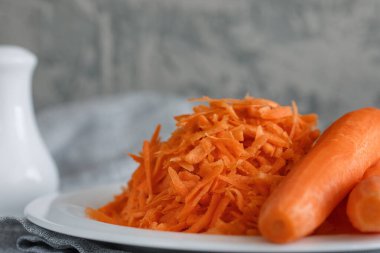 Beyaz bir tabakta rendelenmiş havuç ve yanında iki havuç.