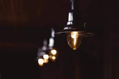 Karanlık bir odada, teneke abajurlu, yanan ampul.