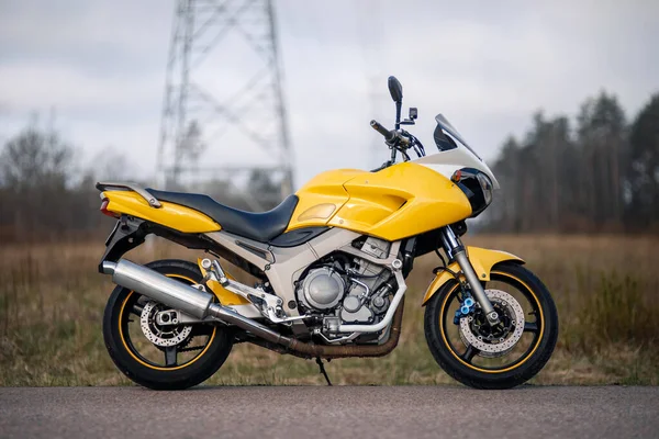 Yol kenarındaki sarı motosikletin yan görüntüsü.