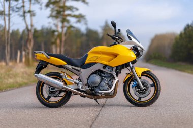 Orman bölgesinde sarı bir motosikletin yan görüntüsü.