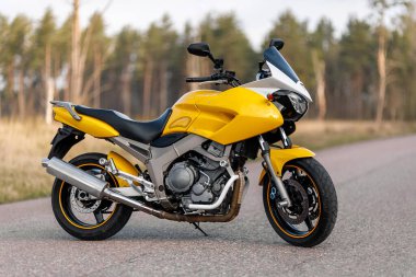 Orman bölgesinde sarı bir motosikletin yan görüntüsü.