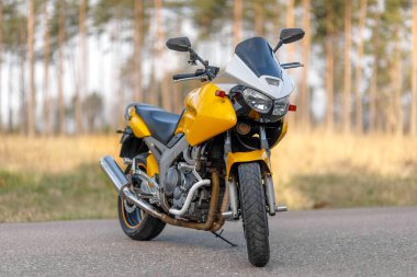 Sarı motosiklet yolda, orman bölgesinde, ön taraf manzaralı.