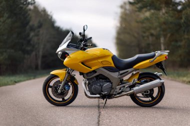 Orman bölgesinde sarı bir motosikletin yan görüntüsü.