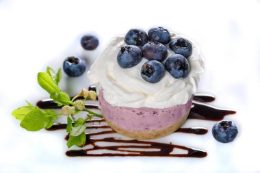 Taze böğürtlenlerle süslenmiş yaban mersinli yoğurt keki ve beyaz bir masada yeşil yaban mersini filizleri.