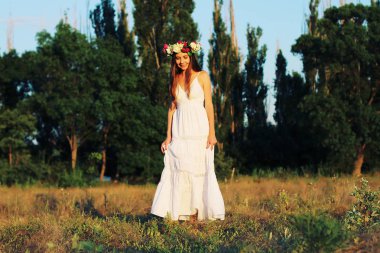 Beyaz elbise ayakta çiçek taç giyen alanında kadında. 