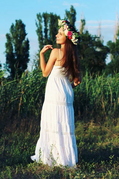 Frau in weißem Kleid steht mit Blumenkrone auf Feld. — Stockfoto