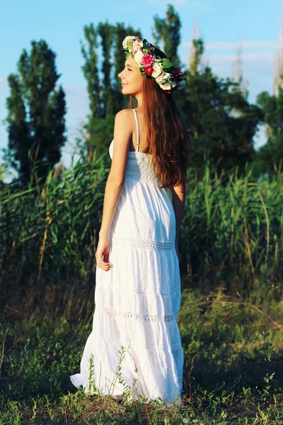 Femme en robe blanche debout dans le champ portant la couronne de fleurs . — Photo