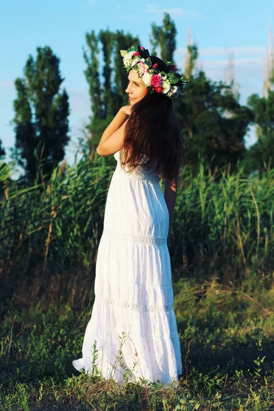 Frau in weißem Kleid steht mit Blumenkrone auf Feld. — Stockfoto
