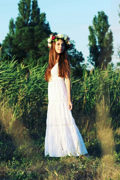 Donna in abito bianco in piedi in campo indossando fiore corona . — Foto Stock