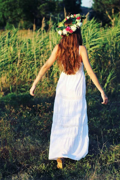 Vrouw in een witte jurk reputatie op gebied dragen bloem kroon. — Stockfoto