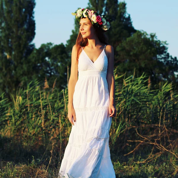 Femme en robe blanche debout dans le champ portant la couronne de fleurs . — Photo