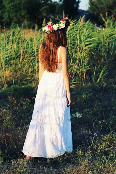 Donna in abito bianco in piedi in campo indossando fiore corona . — Foto Stock