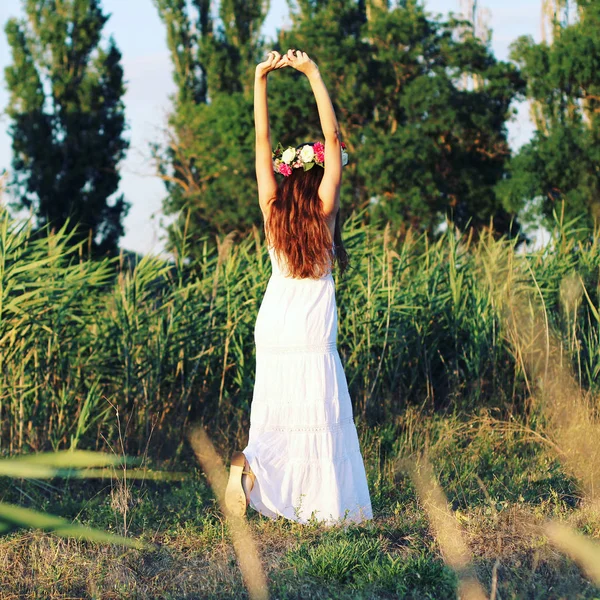 Femme en robe blanche debout dans le champ portant la couronne de fleurs . — Photo