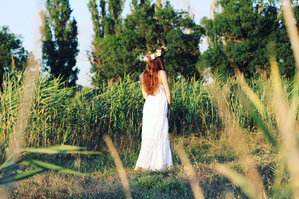 Женщина в белом платье, стоящая в поле в цветочной короне . — стоковое фото