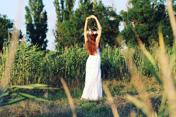 Femme en robe blanche debout dans le champ portant la couronne de fleurs . — Photo