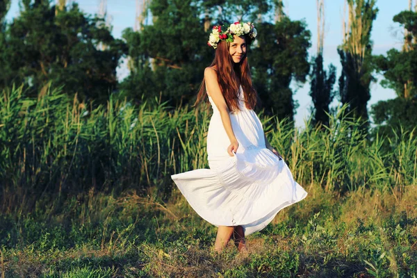 Vrouw in een witte jurk reputatie op gebied dragen bloem kroon. — Stockfoto