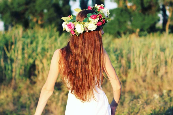 Vrouw in een witte jurk reputatie op gebied dragen bloem kroon. — Stockfoto