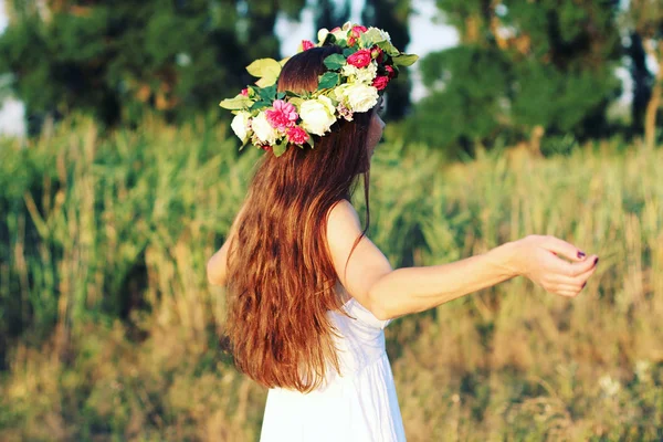 Mulher de vestido branco em pé no campo usando coroa de flores . — Fotografia de Stock