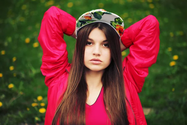 Giovane ragazza bruna in cap posa contro verde erba sfondo . — Foto Stock