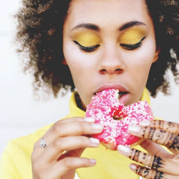 Mulher em suéter amarelo mordendo donut — Fotografia de Stock