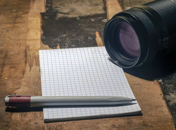 A camera lens and a blank notebook.