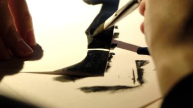 Bir insan bir kağıt parçasına siyah boya çizer.