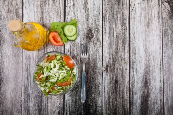 Salada fresca, garfo e óleo vegetal estão em uma mesa de madeira — Fotografia de Stock