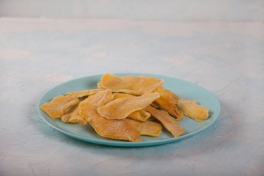 Hafif arka planda mavi bir tabakta doğal mango cipsi. Yatay olarak