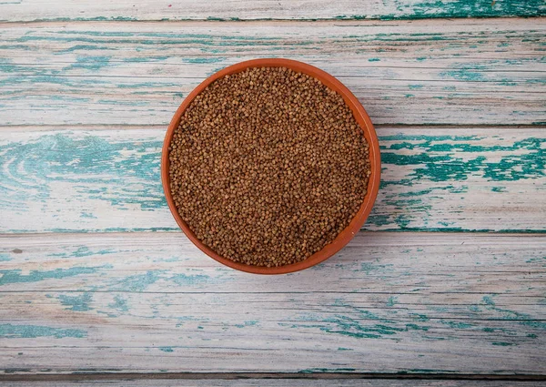 Raw buckwheat in a clay cup on a blue wooden background. Copy spaes. — Stock Photo, Image