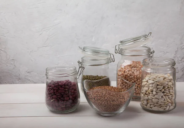 Raw red and white beans, mung bean, yellow peas and buckwheat sprinkled in a glass jar stand on a white wooden background/ Copy spaes