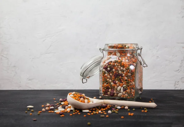 Beans, white and red, lentils green and red, peas in a glass jar on a black table on a white background. Sprinkled beans and wooden spoon. Healthy eating. Vegetarianism — Stock Photo, Image