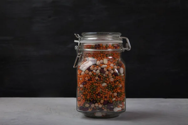 하얀 탁자 위에 놓여 있는 뚜껑 이 없는 유리병 안에 하얀 콩 과붉은 콩, 녹색 과 빨간색 렌즈콩이 들어 있다. 건강 한 식생활을 하는 식물. 사본 스파게티. — 스톡 사진
