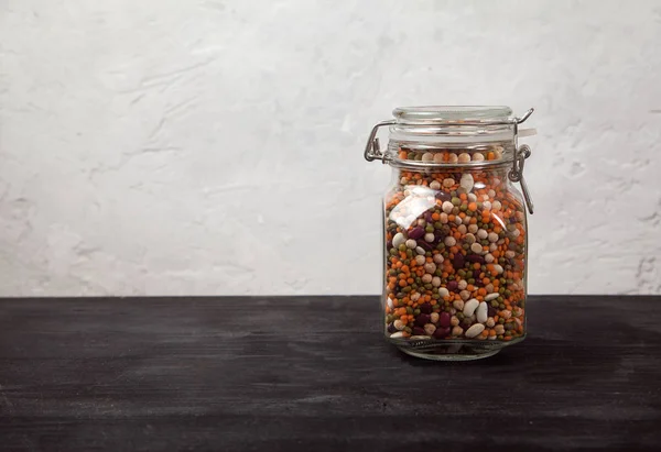 豆、白と赤、レンズ豆緑と赤、白い背景に黒いテーブルの上にガラス瓶にエンドウ豆。コピースペース — ストック写真