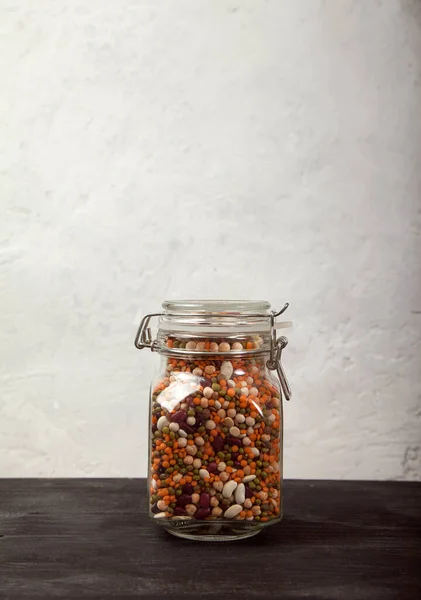 豆类，白色和红色，扁豆绿色和红色，豌豆在一个封闭的玻璃瓶在一个黑色桌子上的白色背景。顶层产卵. — 图库照片