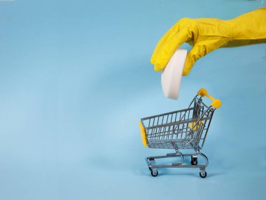 Sarı eldivenli bir kadın bir kalıp sabunu mavi arka planda süpermarket tramvayına batırıyor. Dezenfeksiyon, Coronvirus. covid 19. Kopyalama maçları.