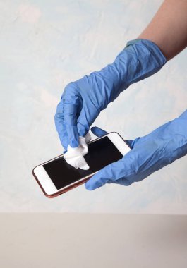 Beyaz arka planda beyaz bir dezenfektan mendille akıllı telefonu ovuşturan bir kadın eli. Dezenfekte. - Güvenlik. Dikey. Kürekleri kopyala