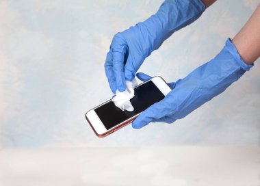 Beyaz arka planda beyaz bir dezenfektan mendille akıllı telefonu ovuşturan bir kadın eli. Dezenfekte. - Güvenlik. Saflık. Kürekleri kopyala